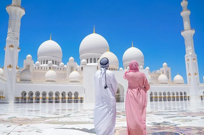 Zwei Besucher von hinten im Innenhof der Moschee, ein Mann in einer weißen Kandura und eine Frau in einer rosa Abaya